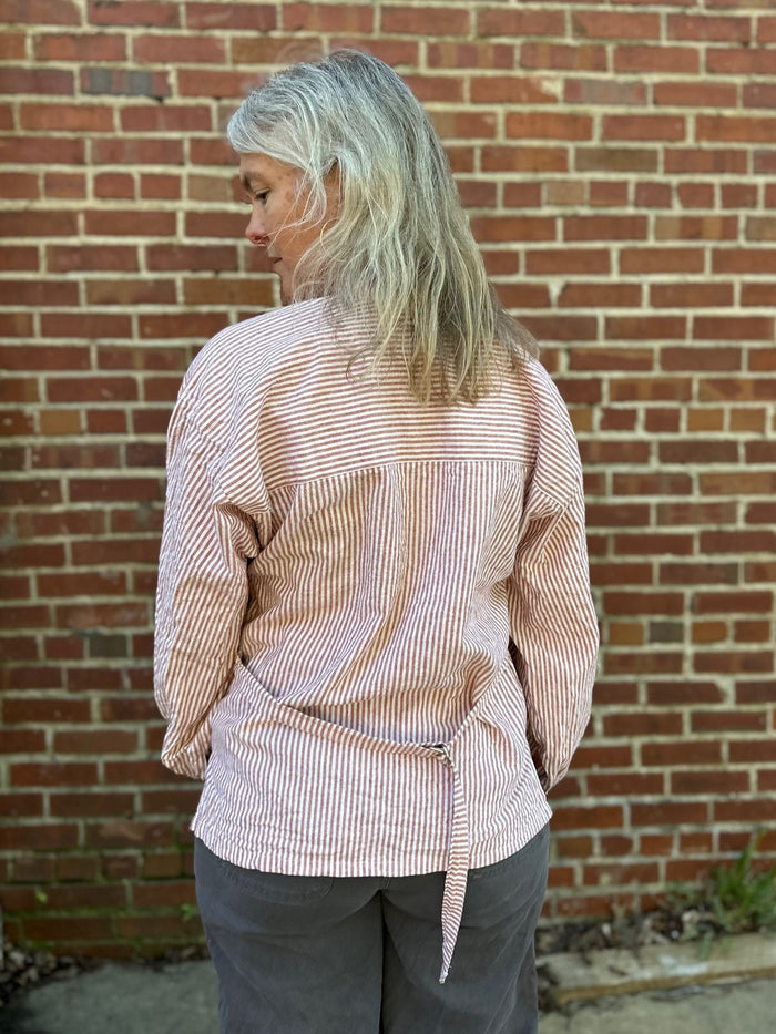 Person wearing a pink and white striped shirt against a brick wall. Back to camera