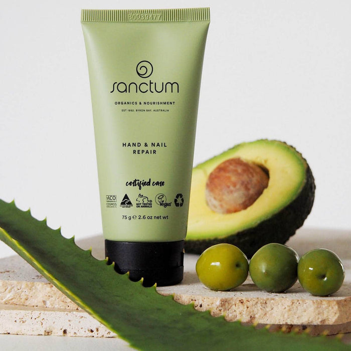 Sanctum Hand & Nail Repair cream with avocado and aloe vera leaves on a light background.