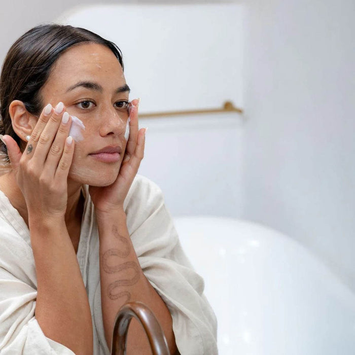 Woman applying cream to her face in a bathroom setting.