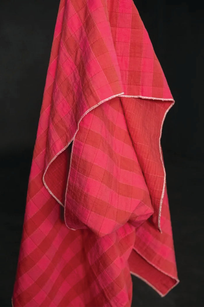 A quilted cotton jacquard fabric with a checkered pattern on red and fuchsia, on a dark grey background.