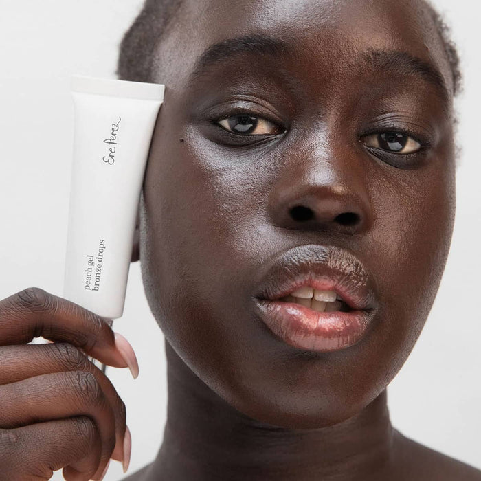 Person holding Ere Perez Peach Gel Bronze Drops 30ml product with a neutral background.