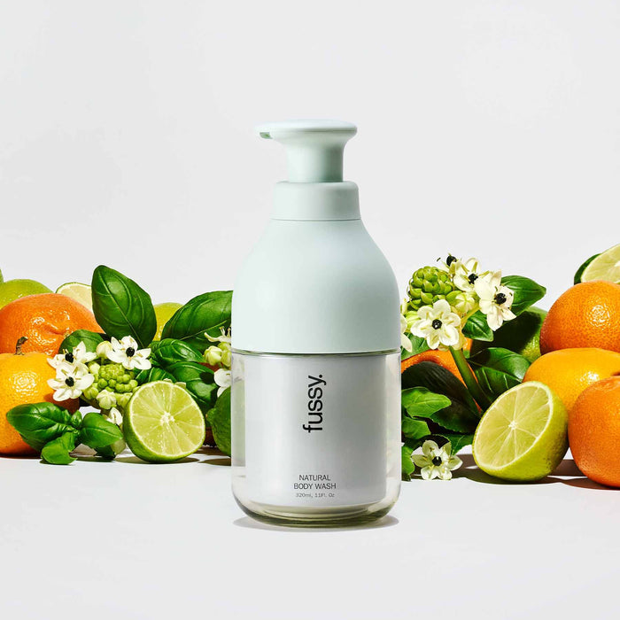 Fussy's Tropic Tonic natural body wash pump bottle, set against a background of limes, mandarins and basil leaves.