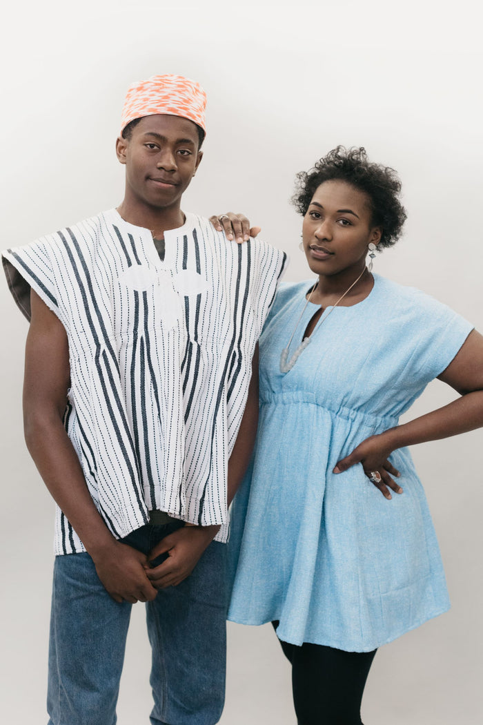 An African American young man and women standing in front of a white studio backdrop wearing the Ghanaian Smock.