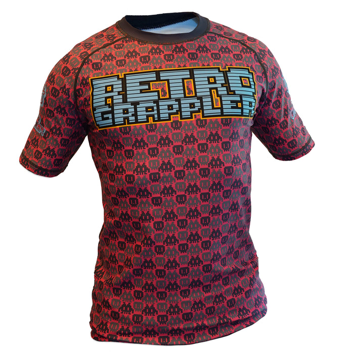 The Retro Grappler 8-Bit Pink Rash Guard features a black pixelated 8-bit design and RETRO GRAPPLE in bold, colorful letters on the chest. Its moisture-wicking fabric keeps you cool and dry during workouts.