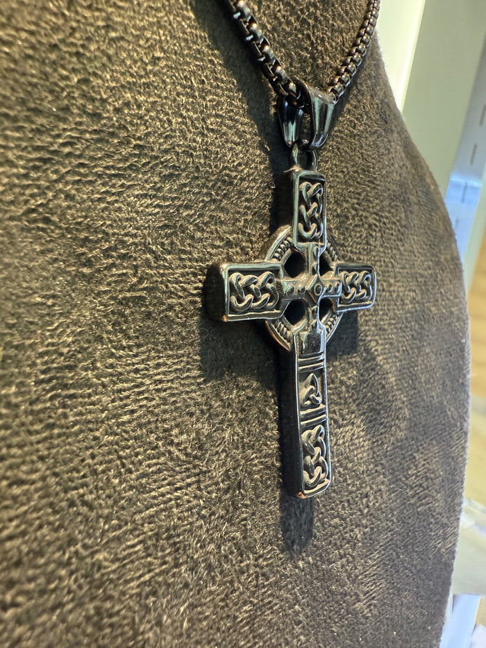 Black cross pendant on a chain against a textured brown background