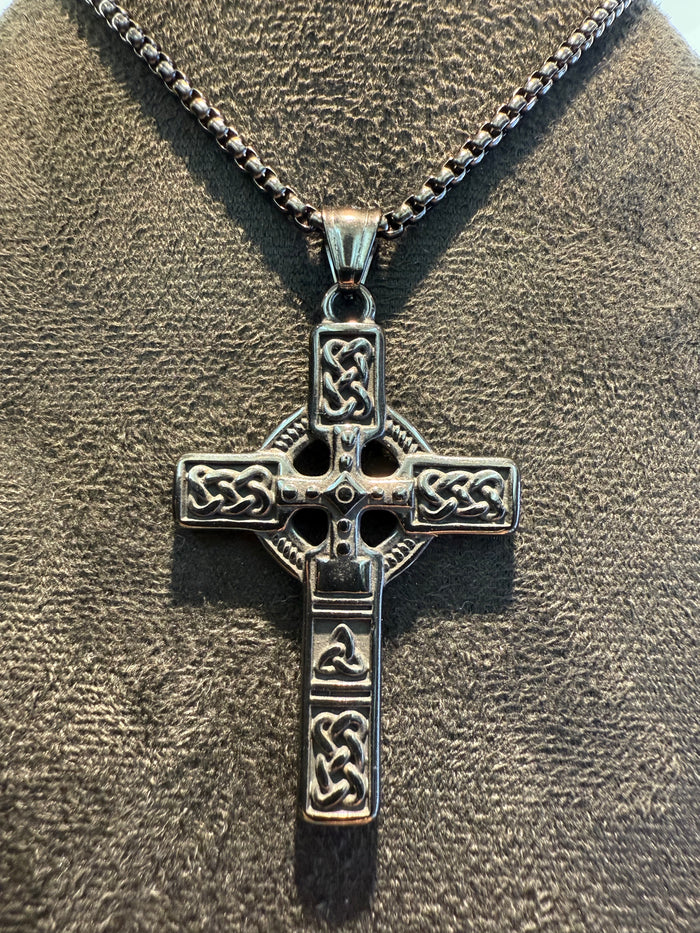 Black Celtic cross pendant on a chain against a textured brown background