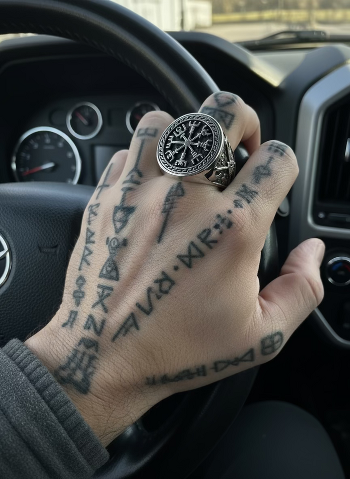 Hand with tattooed fingers wearing a large ring inside a car.