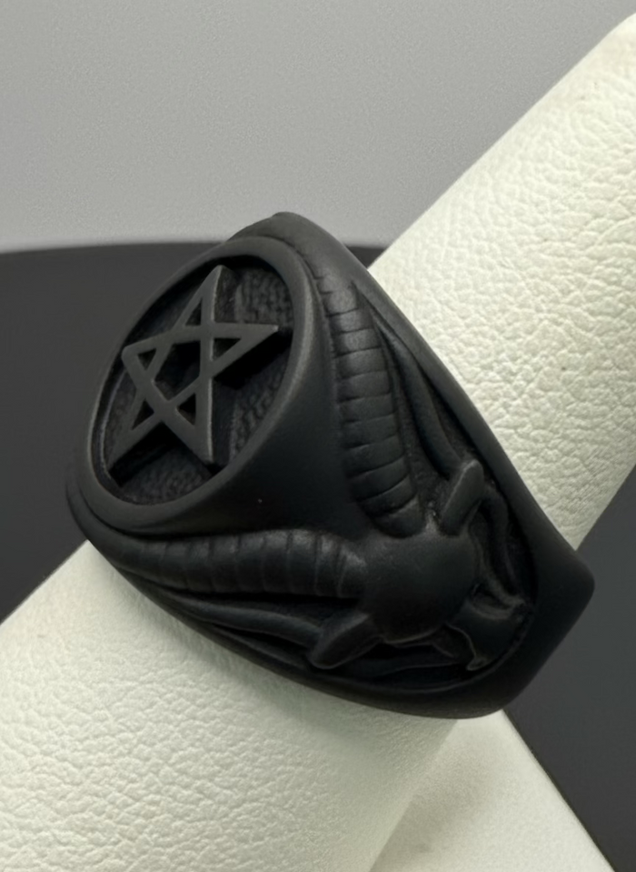 Black titanium ring with pentagram design on a white stand against a gray background