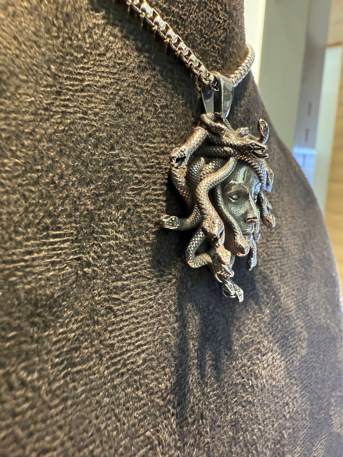 Titanium Medusa pendant on a chain against a textured brown background