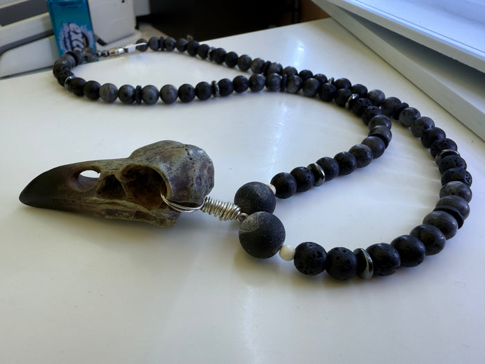 Necklace with black beads and a bird skull pendant on a white surface