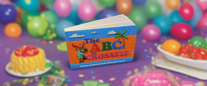 The ABCs Of Childrens Book Bundle by Retro Grappler stands upright on a table, surrounded by balloons and treats—a festive scene perfect for young fitness fans.