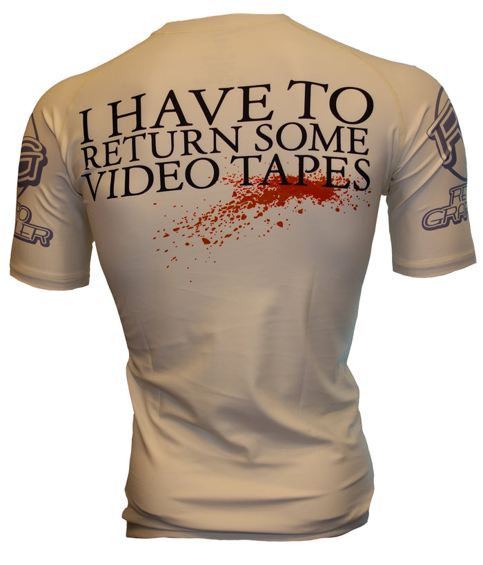 The Retro Grappler American Grappler Rash Guard features bold black “I HAVE TO RETURN SOME VIDEO TAPES” text and a red blood splatter graphic on the back—perfect for MMA fans.