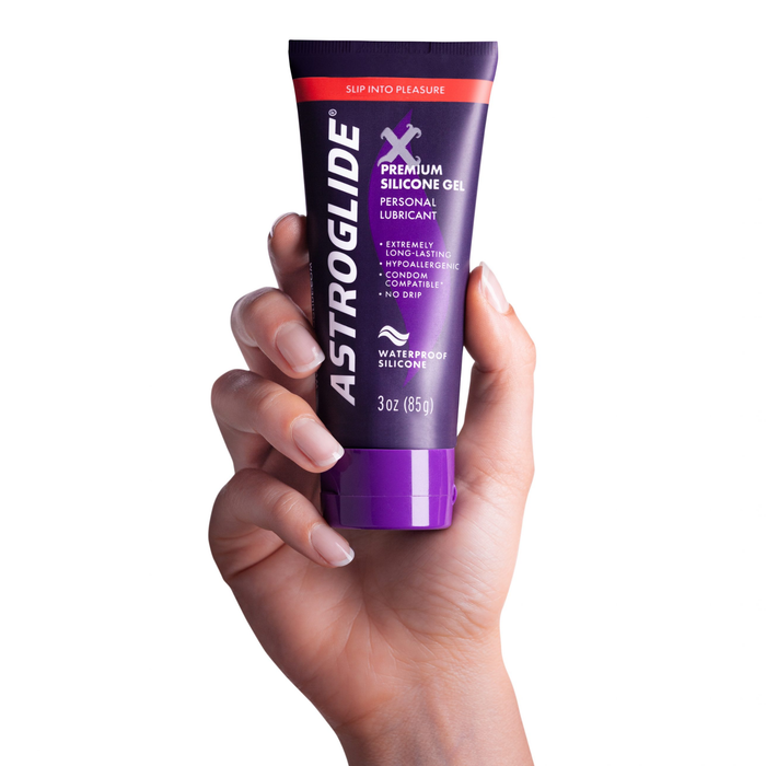 A hand holding a purple tube of Astroglide X Premium Silicone Gel Personal Lubricant, 3 oz (85g).
