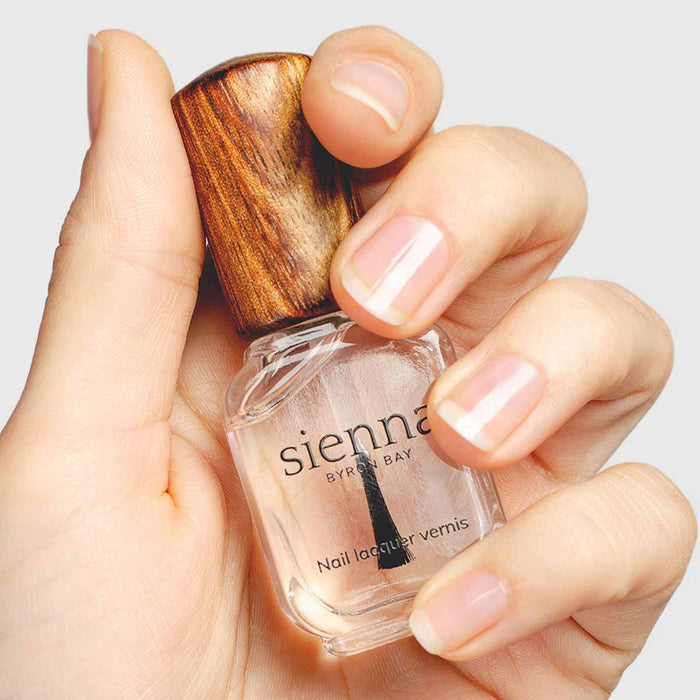 Hand holding a bottle of Sienna nail polish with a wooden cap on a light background.