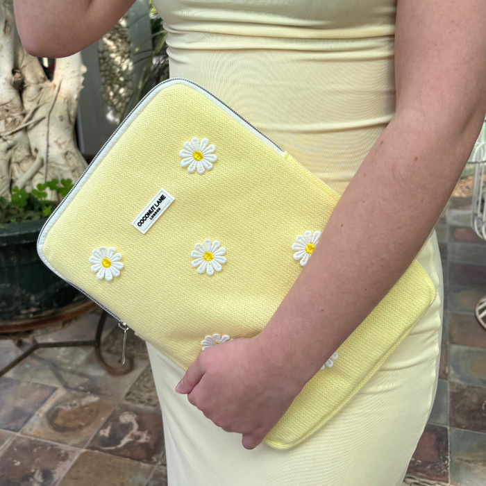 Yellow-dressed person holding Coconut Lane Buttercup Bloom iPad sleeve with white embroidered daisy pattern.