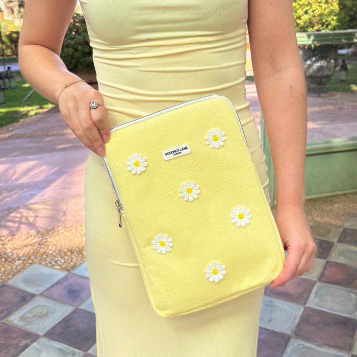 Woman in yellow dress holds Coconut Lane Buttercup Bloom iPad Sleeve and matching daisy pouch outdoors.
