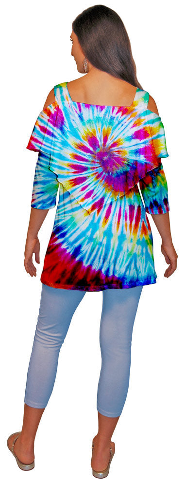 Back view of a woman wearing a colorful tie-dyed shoulder cut out top and light blue capri leggings on a white background.