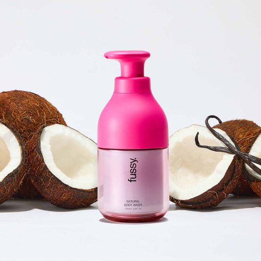 Fussy's natural, refillable Coconut Milk body wash in a bright pink pump bottle, set against a background of coconuts and vanillla pods.