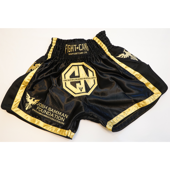 The Combat Night Black Gold Premium Muay Thai shorts feature black and gold colors, the Josh Samman Foundation logo, fightcamp.com, an MMA emblem, and a Combat Night reference printed on the front.