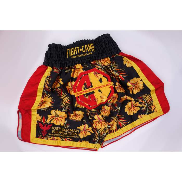 The Combat Night Black Gold Red Hawaiian Style Muay Thai shorts feature a black base, yellow hibiscus flowers, red and yellow accents, and Combat Night logos on the waistband and leg.