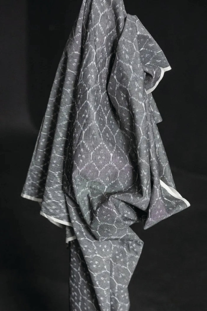 The warp and weft of this ikat is in black and white threads which results in a soft grey colour with a white geometric pattern. On a dark grey background