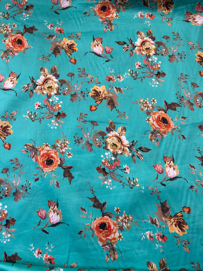 A close-up of a teal fabric with an all-over floral print featuring orange, pink, and brown flowers with green and brown leaves.