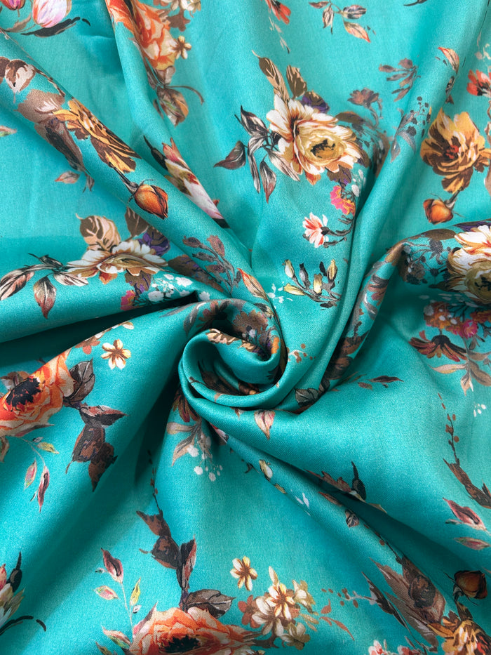 A close-up of a teal fabric with a vintage floral print in shades of orange, brown, cream, and white, styled in a central swirl drape.