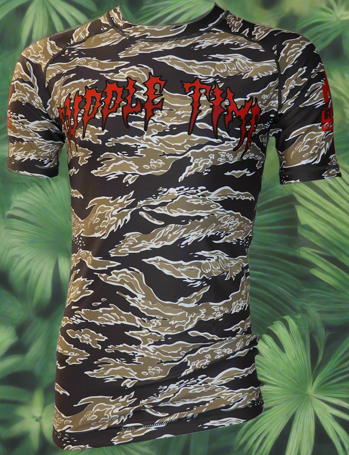 The Retro Grappler Cuddle Time Tiger Stripe Camo Rash Guard features a fitted short-sleeve design with brown, black, and white stripes, red CUDDLE TIME text on the chest, and a green tropical leaf background—ideal for BJJ rash guard collectors.