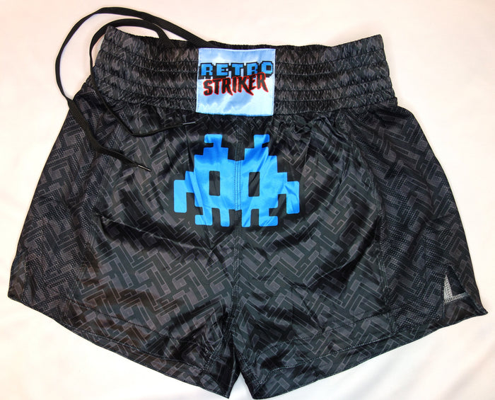 The Retro Grappler Dark Labyrinth Muay Thai Shorts feature a blue pixelated alien graphic, RETRO STRIKER patch on the waistband, geometric pattern, lightweight feel, 5 inseam, and a small logo on the leg.