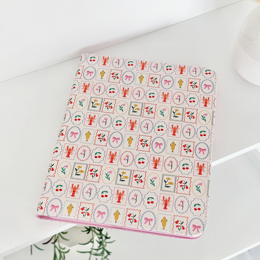 Dolce Vita iPad case with a colorful pattern on a white shelf next to a patterned notebook and small green plant.