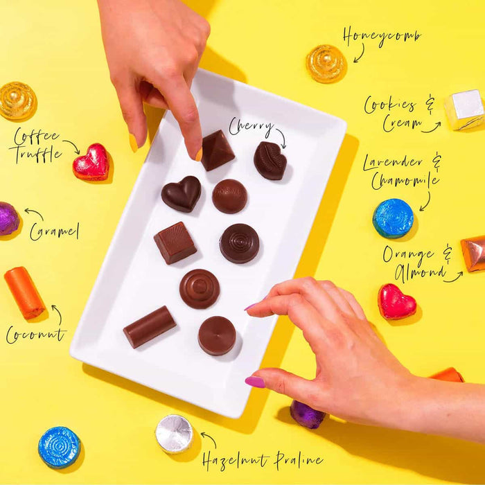 Assorted chocolate candies on a white tray with labelled flavours on a yellow background.
