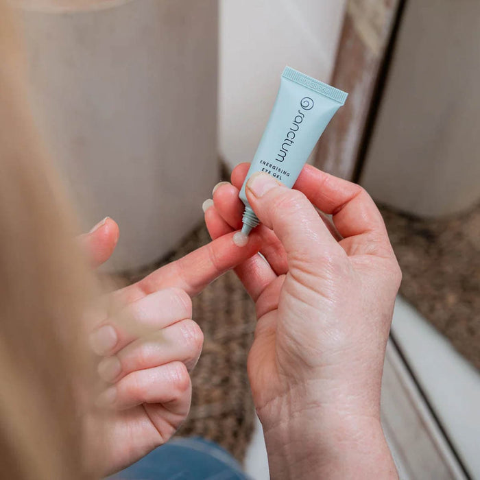 Person holding a small blue tube of eye gel with a blurred background.