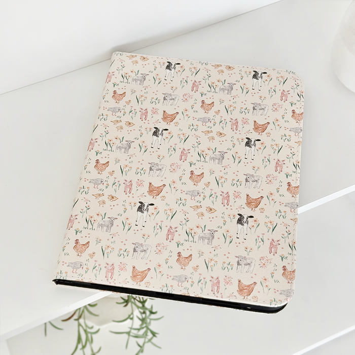 Coconut Lane Farmyard Friends iPad case with floral pattern on white shelf next to a green potted plant.