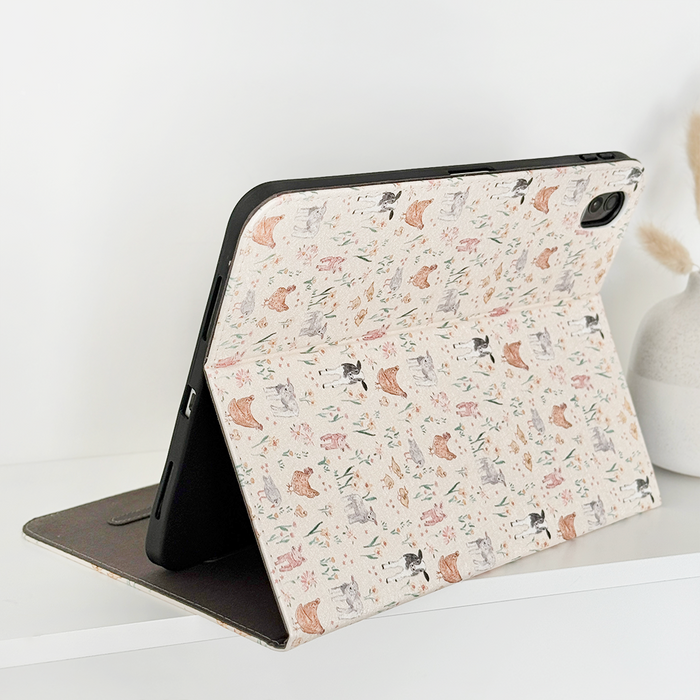 Farmyard Friends iPad case with playful animal pattern holds an iPad on a white shelf next to dried flowers in a vase.