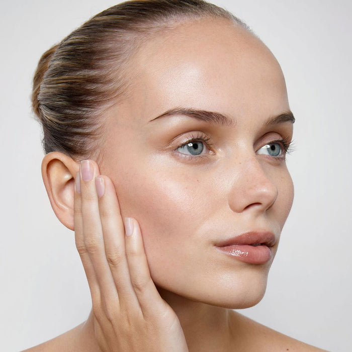 Woman touching her face with a neutral background.