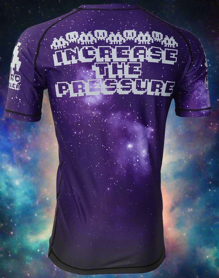 The Retro Grappler Galaxy Increase the Pressure Rash Guard features pixelated alien graphics and bold white text on a purple galactic background—ideal for MMA or jiu jitsu training with standout space-inspired style.