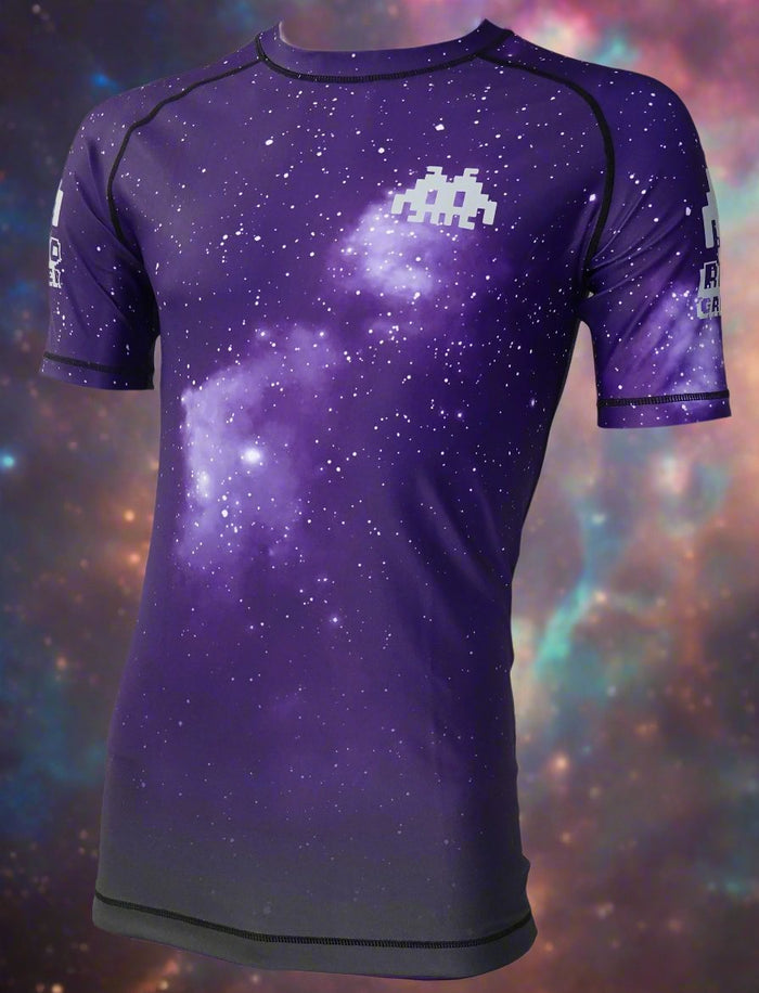 The Retro Grappler Galaxy Increase the Pressure Rash Guard is a short-sleeved athletic shirt with a purple galaxy and white star design, featuring a pixelated alien on the chest, inspired by MMA and jiu jitsu rash guards.