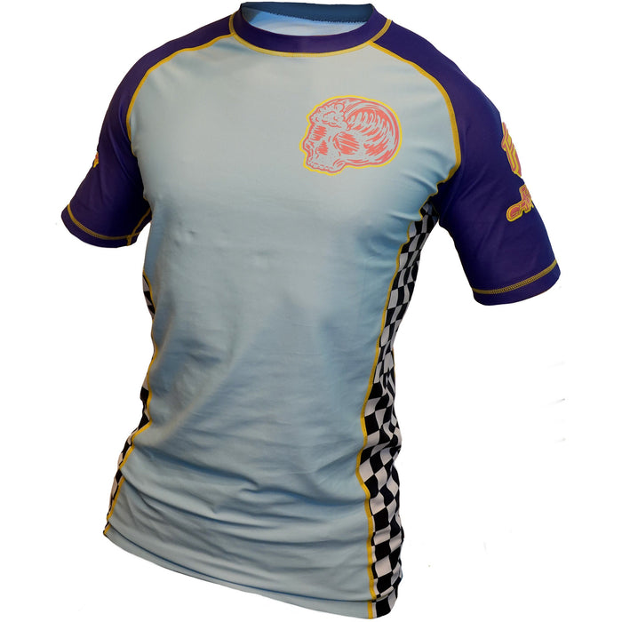 The Retro Grappler Gnarly Surf Rash Guard is a short-sleeve jiu jitsu top featuring a light blue front, dark blue sleeves, yellow trim, black-and-white checkered side panels, and a bold red skull graphic on the chest.