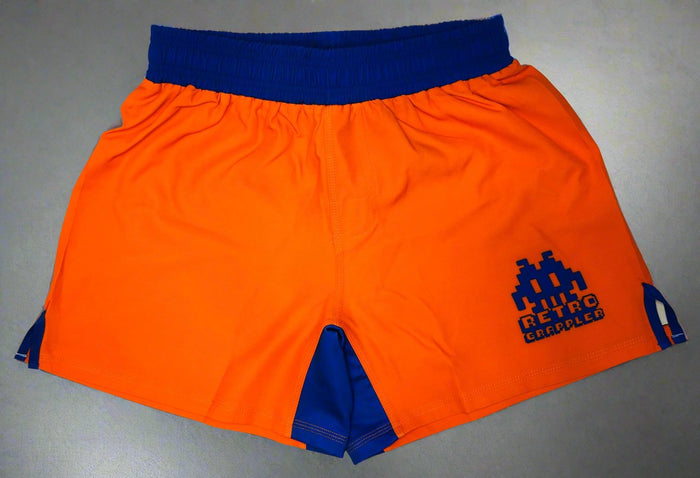 Displayed flat, the Goku Dragon Ball Grappling Shorts by Retro Grappler feature bright orange lightweight fabric, a blue waistband and inner lining, plus a blue pixelated Retro Grappler logo on the left leg for vintage video game style.