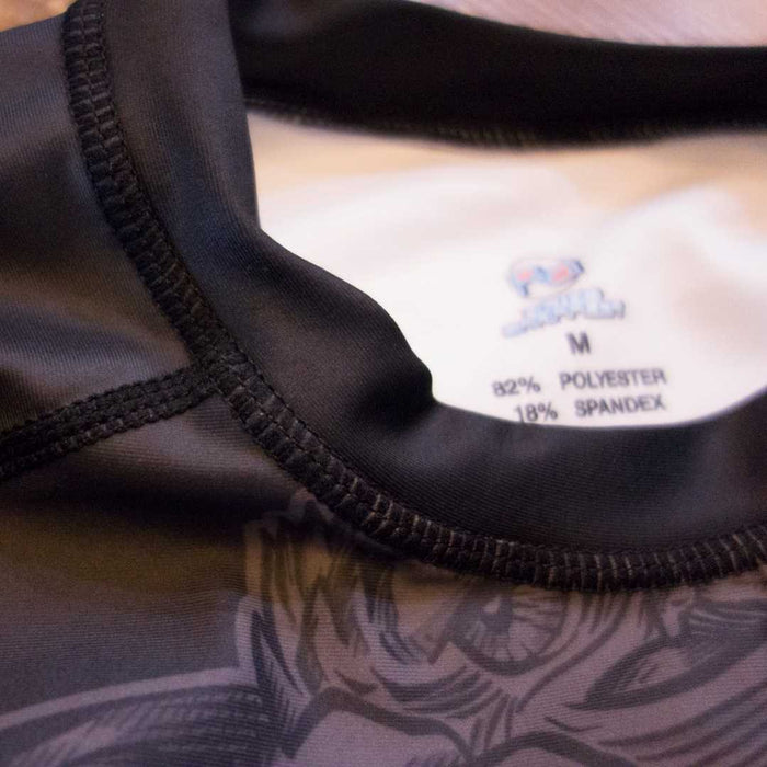 Close-up of the Golden Waves BJJ Rash Guard by Retro Grappler, highlighting its black and white collar, inside tag (82% polyester, 18% spandex), and part of the abstract design—perfect for jiu jitsu training.