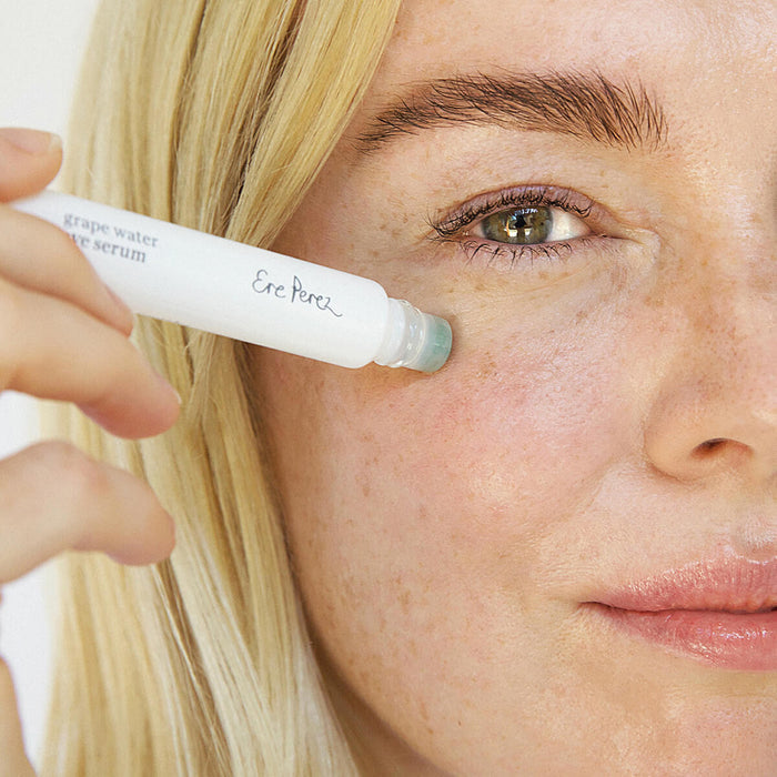 Woman using Ere Perez Grape Water Eye Serum with a jade roller applicator.