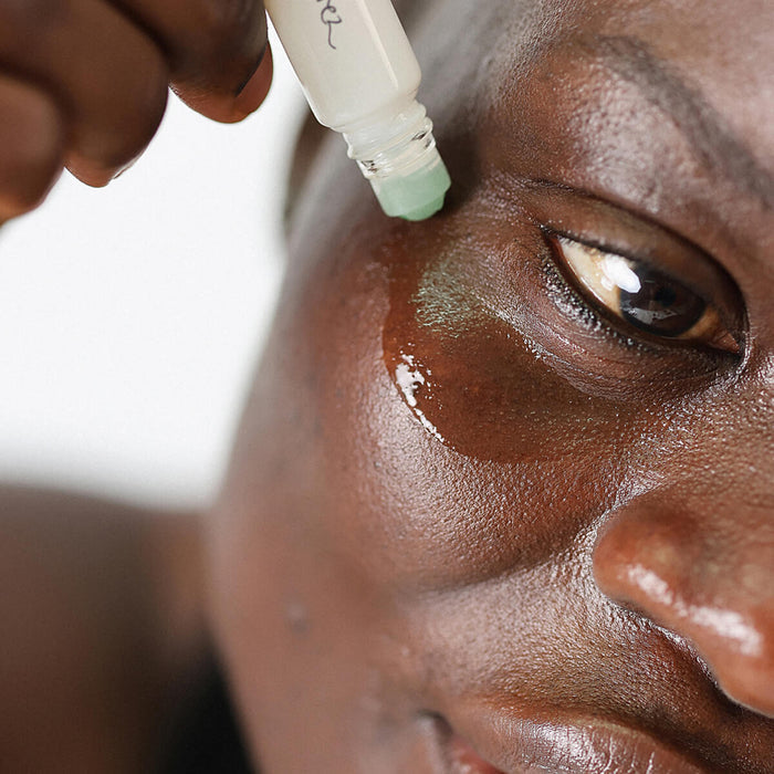 Woman using Ere Perez Grape Water Eye Serum with a jade roller applicator under the eye area.