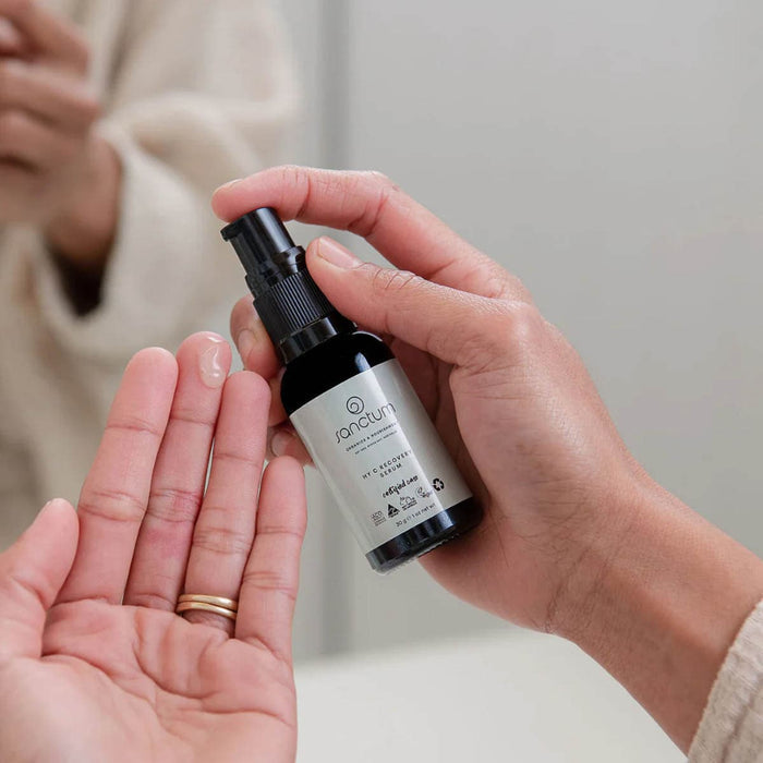 Person holding a bottle of serum with another hand open palm up.