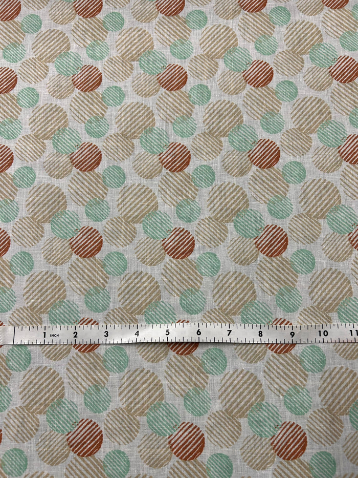 Linen fabric with a a retro abstract polka dot print fabric in mint, beige, and rust on an ivory background. The circles vary in size and are filled with fine diagonal stripe textures, creating a layered geometric look with a hand-printed feel and a ruler for scale