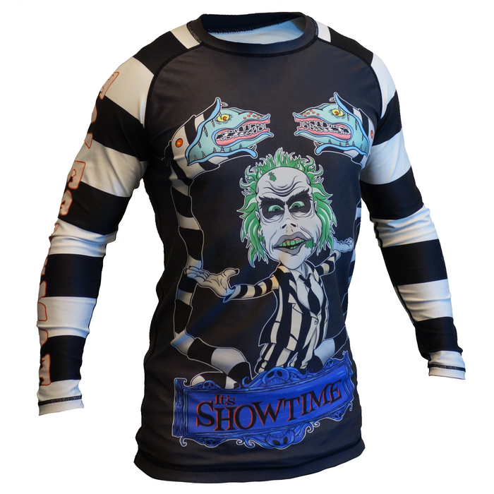 The Retro Grappler Its Showtime Beetle Juice Rash Guard is a black-and-white striped, long-sleeve shirt made from four-way stretch polyester spandex. It features a green-haired cartoon character with snake arms and Its Showtime in blue at the bottom.