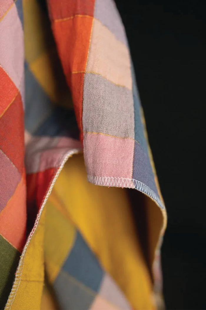 Close up of a colorful checked print of yellow, oranges, blues, purples, and pinks on a black background
