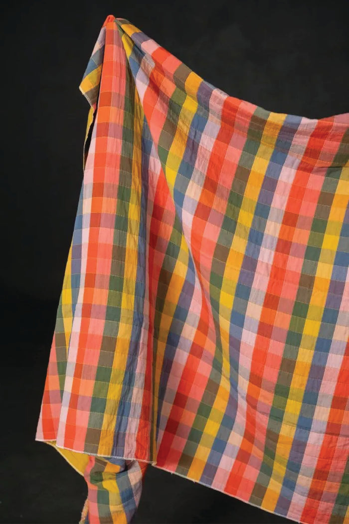 Colorful checked print of yellow, oranges, blues, purples, and pinks hung out on a black background