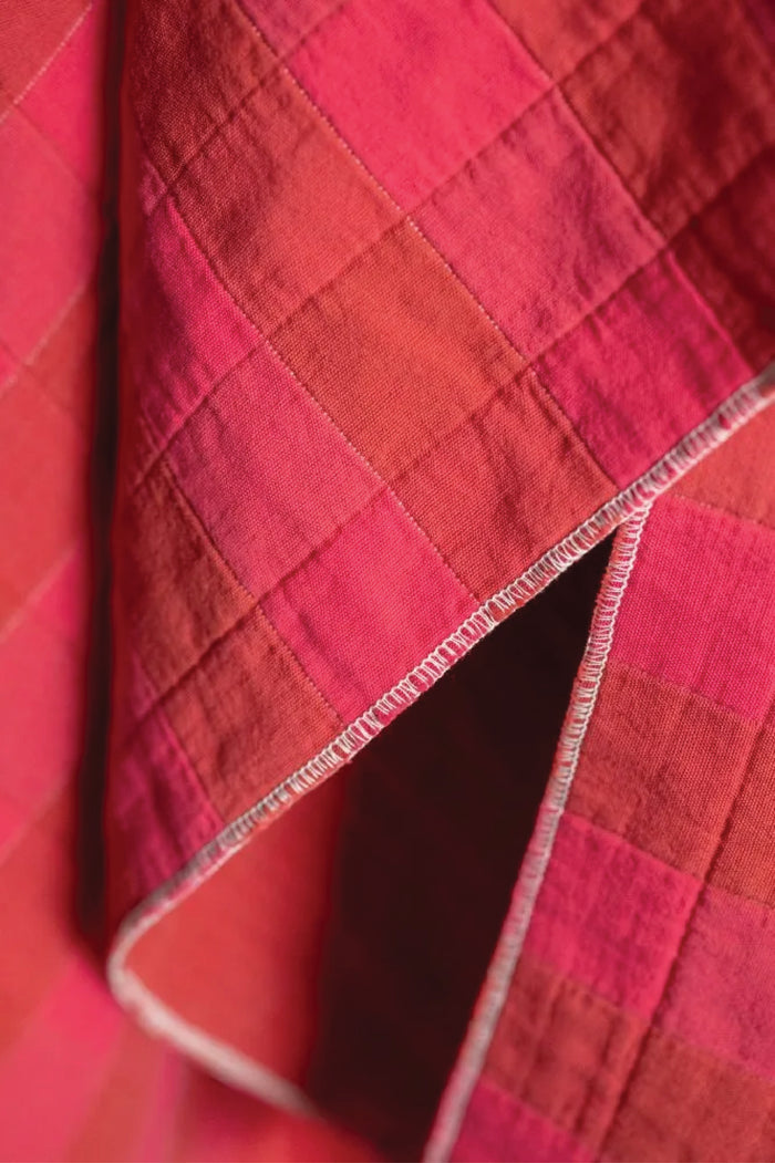 Close-up of a quilted cotton jacquard fabric with a checkered pattern on red and fuchsia.
