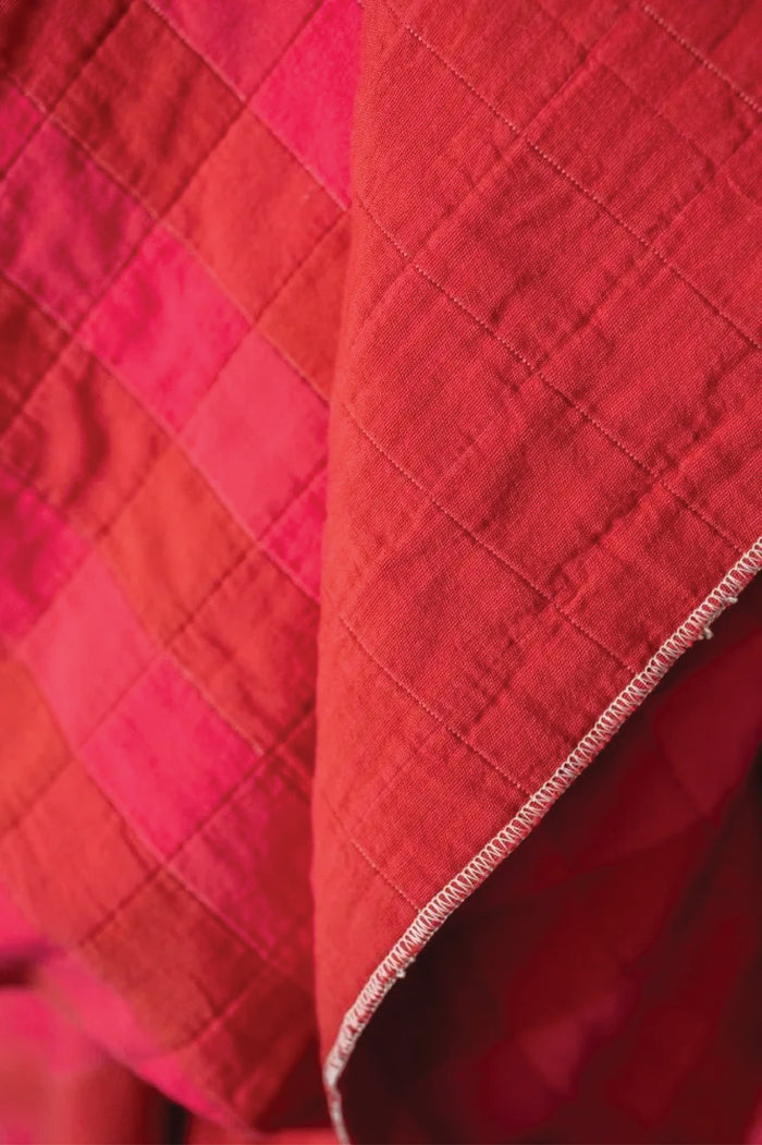 Close-up of a quilted cotton jacquard fabric with a checkered pattern on red and fuchsia.