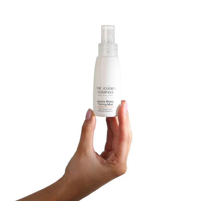 Hand holding a bottle of The Jojoba Company Water Toning Mist on a white background